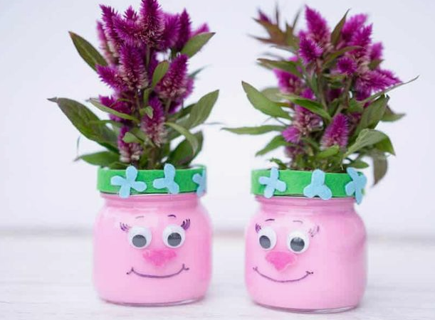 25 Easy DIY Home Decor Crafts That Look Stylish "Two pink painted glass jar vases decorated with googly eyes, smiling faces, and green felt bands, holding vibrant purple flowers as part of 25 easy DIY home decor crafts for kids' rooms."