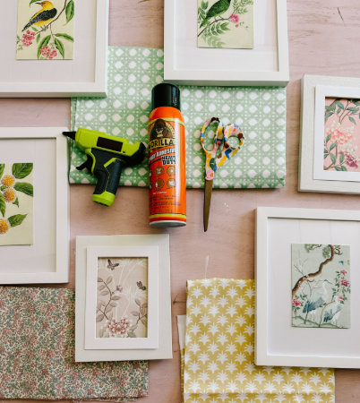 A flat lay showing white picture frames, fabric pieces, scissors, a glue gun, and adhesive spray arranged for upcycling projects, showcasing creative DIY crafts with old clothes.