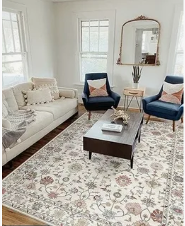 Vintage Modern Home Decor Ideas: 15 Ways to Mix Old and New "Bright living room highlighting Vintage Modern Home Decor Ideas, featuring a cream-colored sofa, dark blue accent armchairs, an ornate vintage gold wall mirror, a dark wooden coffee table, and a large patterned area rug."