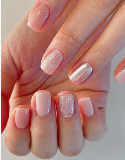 Close-up of nail designs for short nail beds featuring a mix of glossy neutral pink nails, a glitter accent nail, and a reflective chrome accent nail on short, squared-rounded nails.