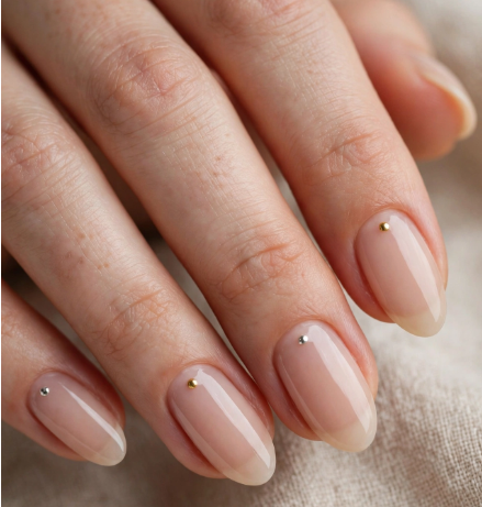 Minimalist metallic stud nail art for beginners featuring alternating tiny gold and silver dots near the cuticle on sheer nude oval nails.   