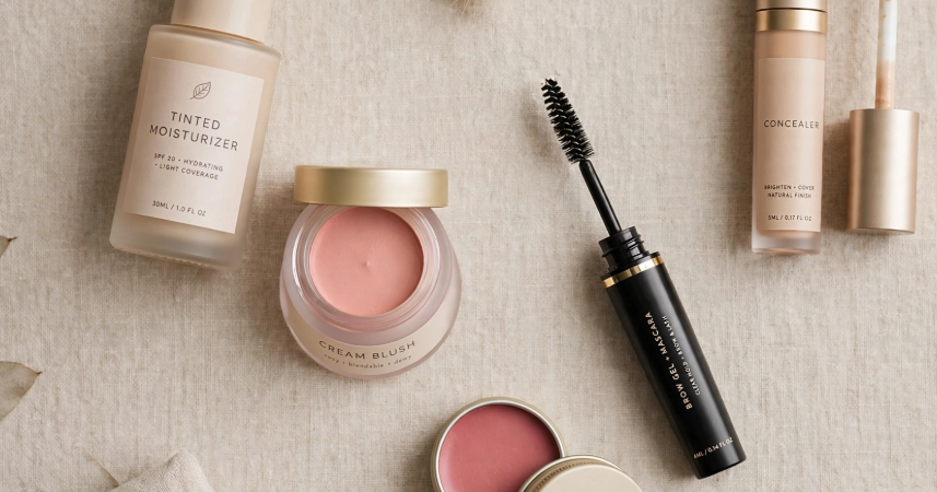 Makeup Routine With Only 5 Products: A Minimal Beginner Guide Flat lay of a minimal makeup routine with only 5 products including tinted moisturizer, concealer, cream blush pot, brow gel and mascara, and tinted lip balm tin.