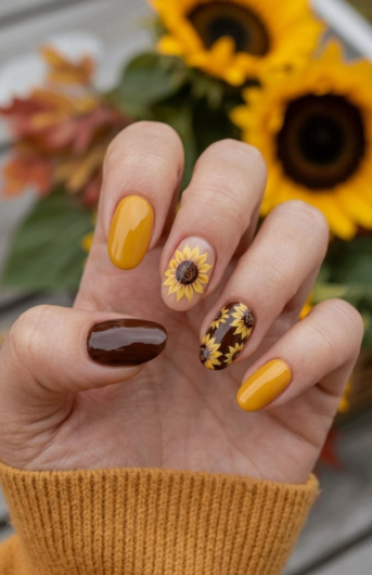 24 Sunflower Nail Ideas for a Bright, Cheerful Manicure sunflower nail ideas featuring a mix of solid mustard yellow and dark brown nails alongside accent nails with delicate sunflower illustrations on a nude base and a brown background.