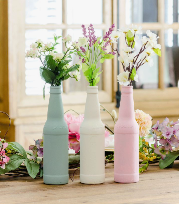 "Three painted glass bottles in sage green, white, and pink holding fresh flowers, featured as part of 25 easy DIY home decor crafts for tabletop styling."
