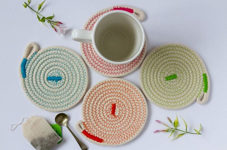 "Handmade coiled rope coasters in pastel colors with colorful zigzag stitching, featured as part of 25 easy DIY home decor crafts for tabletop accessories."