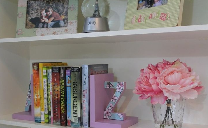 "A styled white bookshelf featuring purple bookends holding books, a decorative letter Z, and a vase of pink peonies, showcased as part of 25 easy DIY home decor crafts for shelf styling."