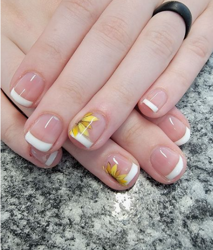 24 Sunflower Nail Ideas for a Bright, Cheerful Manicure sunflower nail ideas featuring classic white French tips on nude nails, with accent fingers showcasing delicate yellow sunflowers painted along the white tips.