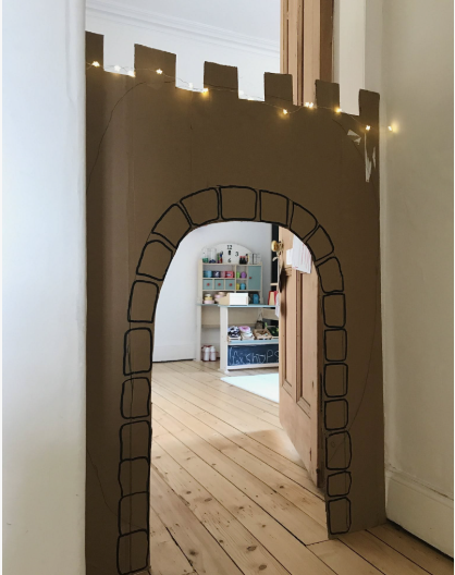 "A doorway transformed into a castle archway using brown cardboard with drawn stone blocks and fairy lights, showcased as part of 25 easy DIY home decor crafts for kids' playrooms."