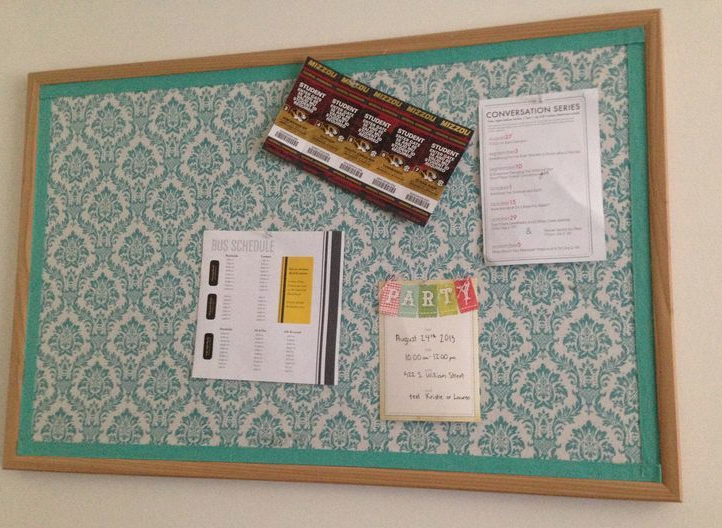 "A custom fabric-covered bulletin board featuring a teal damask pattern and wooden frame, showcasing notes and schedules as part of 25 easy DIY home decor crafts for office organization."