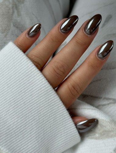 A hand with almond-shaped metallic chrome dark brown nails wearing a white sweater, styled for fall nail ideas 2026.