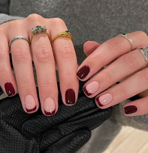 Hands showcasing short, squoval nails with a mix of deep burgundy French tips and solid burgundy polish, styled for fall nail ideas 2026.