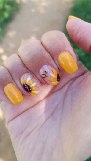 24 Sunflower Nail Ideas for a Bright, Cheerful Manicure sunflower nail ideas featuring solid bright yellow nails paired with accent nails that showcase hand-painted yellow sunflowers and a tiny bumblebee on a sheer nude base.