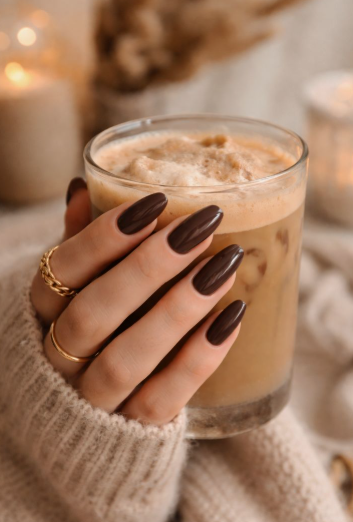 A hand with long, almond-shaped glossy espresso brown nails holding an iced coffee, styled for fall nail ideas 2026.