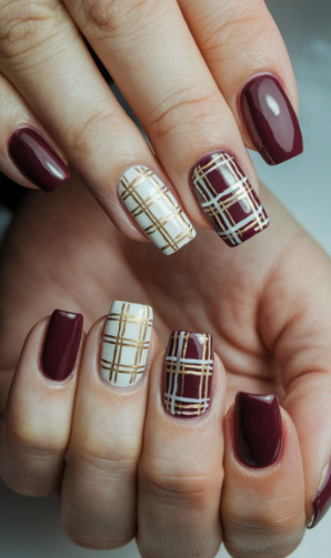 Hands displaying short, squoval nails with solid burgundy and plaid accent patterns, styled for fall nail ideas 2026.