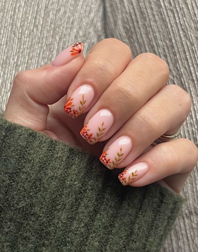 A hand wearing a green sweater showcasing short squoval nails with delicate autumn floral nail art, styled for fall nail ideas 2026.