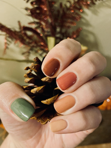 A hand holding a pinecone showcasing short, multi-toned autumn colored nails, styled for fall nail ideas 2026.