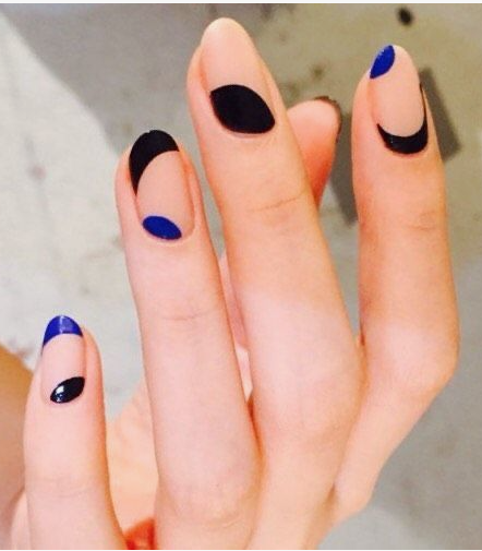 A hand with long, oval-shaped nails featuring abstract black and royal blue negative space art, styled for fall nail ideas 2026.