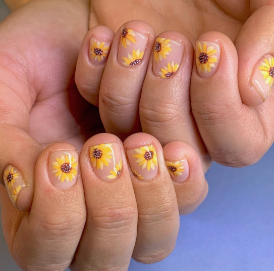 24 Sunflower Nail Ideas for a Bright, Cheerful Manicure sunflower nail ideas featuring short, natural nails with a sheer nude base decorated with scattered hand-painted yellow sunflowers.
