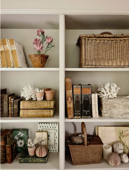 White bookshelves styled with vintage books, wicker baskets, coral decor, and subtle seasonal touches, showcasing elegant fall decor ideas without pumpkins.