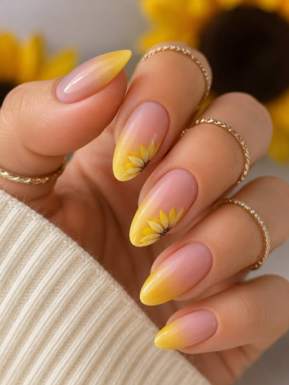 24 Sunflower Nail Ideas for a Bright, Cheerful Manicure sunflower nail ideas featuring almond-shaped nails with a soft nude base and yellow ombre gradient tips, accented with hand-painted yellow sunflowers blooming along the edges.