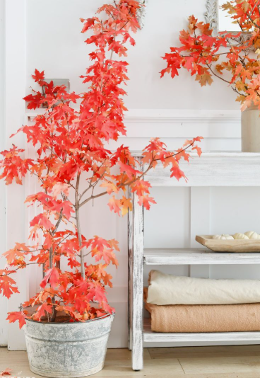 A tall galvanized bucket filled with vibrant red autumn maple branches next to a white console table, highlighting striking fall decor ideas without pumpkins.