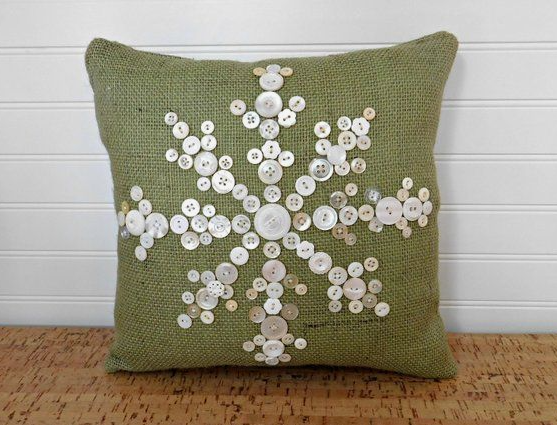 20 DIY Crafts With Old Clothes That Are Easy to Make An olive green burlap throw pillow decorated with a detailed snowflake mosaic made from upcycled white buttons, showcasing creative DIY crafts with old clothes.
