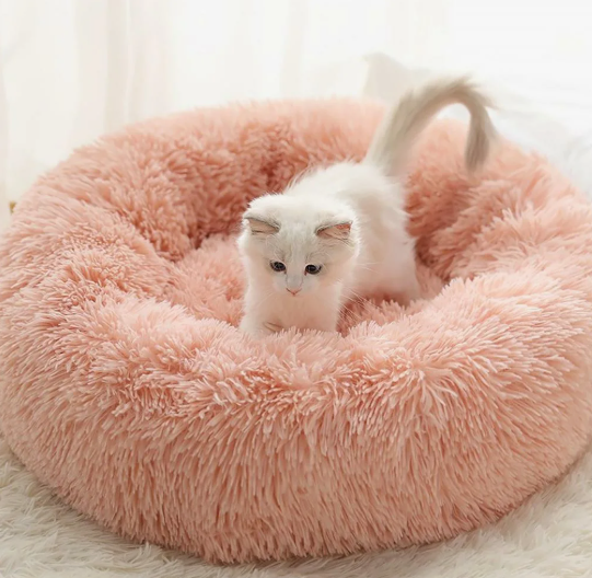 20 DIY Crafts With Old Clothes That Are Easy to Make A fluffy pink donut pet bed with a cute white kitten inside, showcasing creative DIY crafts with old clothes and upcycled faux-fur textiles.