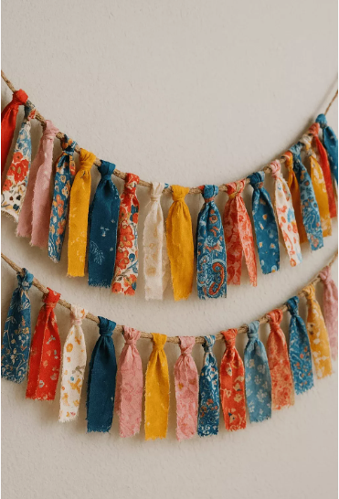 20 DIY Crafts With Old Clothes That Are Easy to Make Two strands of handmade fabric scrap garlands tied with colorful patterned strips, showcasing creative DIY crafts with old clothes for seasonal home decor.