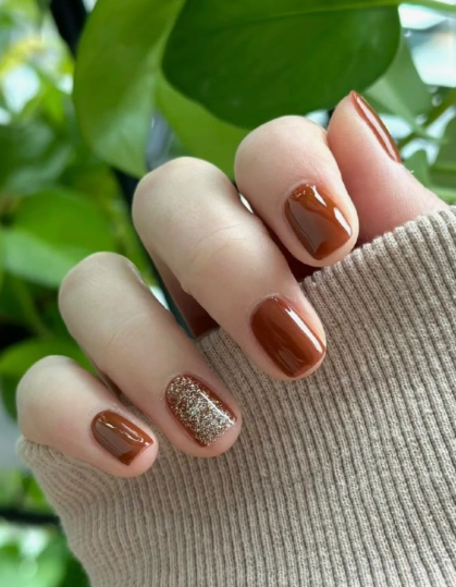 Brown nail ideas for short nails featuring glossy warm amber-brown lacquer with a shimmering gold glitter accent nail on short square nails