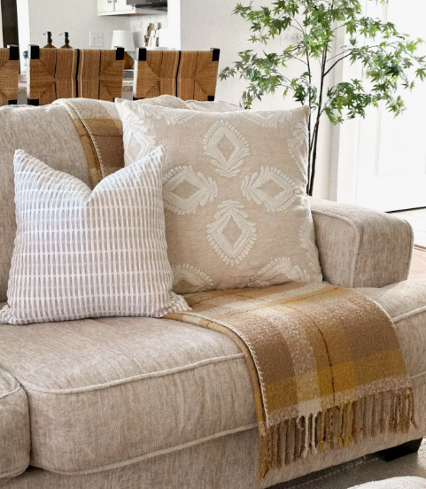 "Cozy home decor ideas for a small apartment featuring a close-up of a neutral beige sofa styled with patterned throw pillows and a warm plaid blanket with fringe."
