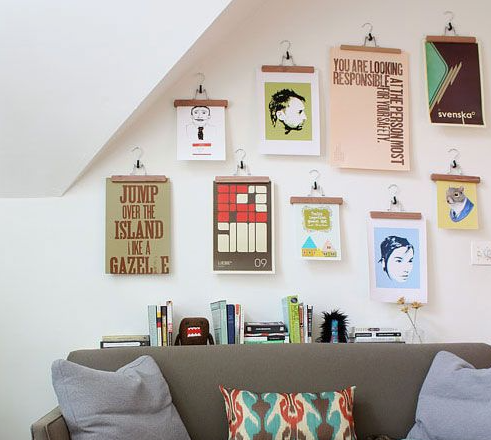 "Cozy home decor ideas for a small apartment featuring a gallery wall of art prints hung with wooden clips above a grey sofa with colorful pillows and stacked books."