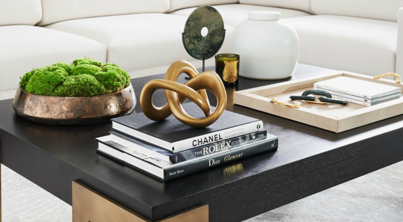 "Cozy home decor ideas for a small apartment featuring a styled coffee table with stacked fashion books, a gold decorative knot sculpture, a moss bowl, and a serving tray."
