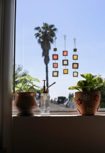 Three translucent hanging suncatchers attached to a window, showcasing creative air dry clay ideas with linked geometric frames in warm tones against a sunny outdoor view.