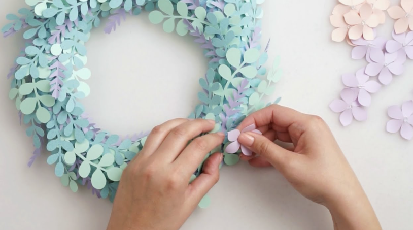 A colorful hanging garland made of pleated accordion paper stars in shades of green, blue, pink, yellow, and light blue, strung together on a thin red cord against a white wall, accompanied by text reading "DIY Paper Star Garland".