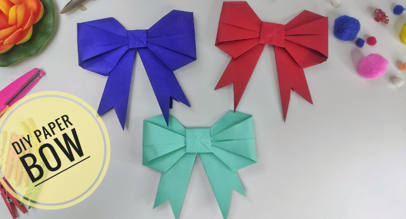 Three handmade decorative paper bows in blue, red, and mint green, featuring neatly folded loops and notched tails, accompanied by a round graphic label reading "DIY PAPER BOW".