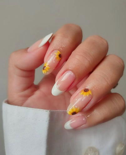 24 Sunflower Nail Ideas for a Bright, Cheerful Manicure sunflower nail ideas featuring almond-shaped nails that combine classic white French tips with sheer nude accent nails showcasing hand-painted yellow sunflowers and tiny white polka dots.