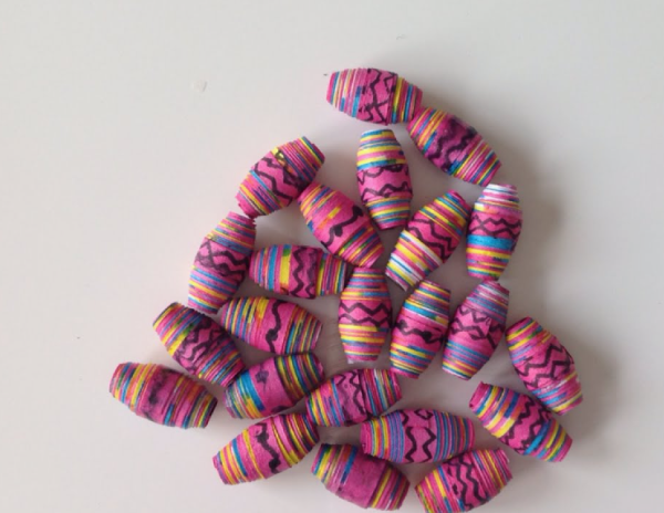 A collection of handmade barrel-shaped paper beads featuring colorful rolled paper stripes and black hand-drawn zig-zag patterns, scattered across a white surface.