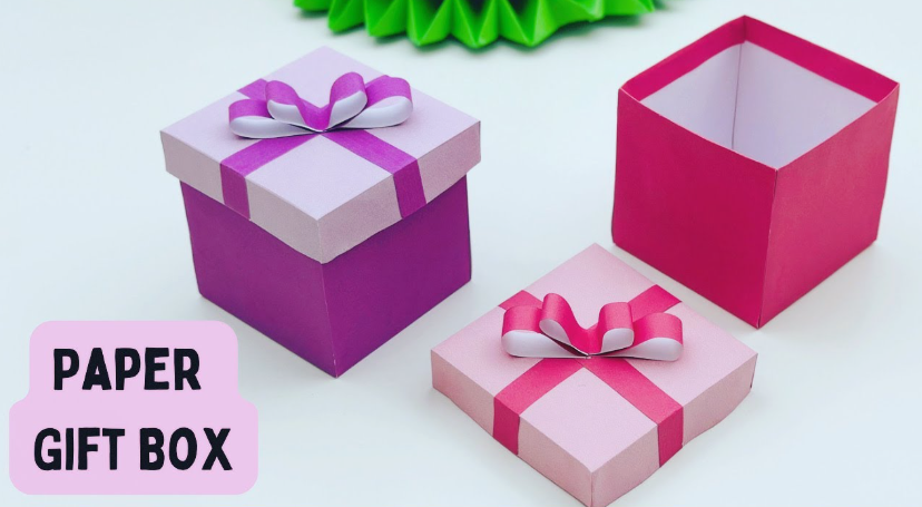 Handmade square paper gift boxes in shades of purple and pink featuring matching ribbon straps and bows on their lids, alongside a label reading "PAPER GIFT BOX"