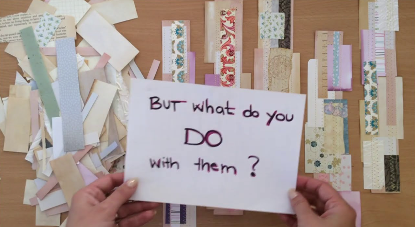 A collection of paper crafting supplies spread across a wooden surface, featuring a large pile of assorted paper scraps on the left, vertically aligned paper strips and journaling tags decorated with patterned washi tape and vintage prints in the background, and a white card held up in the foreground with hand-lettered text reading "BUT what do YOU DO with them ?".