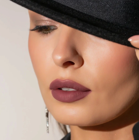 Matte Lipstick Styles in 2026: Modern Looks, Shades & Easy Tips Close-up of a model wearing a dark hat and wearing a sophisticated mauve matte lipstick, highlighting a smooth, velvety texture.