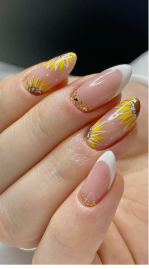 24 Sunflower Nail Ideas for a Bright, Cheerful Manicure sunflower nail ideas featuring almond-shaped nails that combine classic white French tips with gold glitter details at the cuticles, paired with accent nails showcasing hand-painted yellow and white sunflowers on a nude base with tiny white dots.