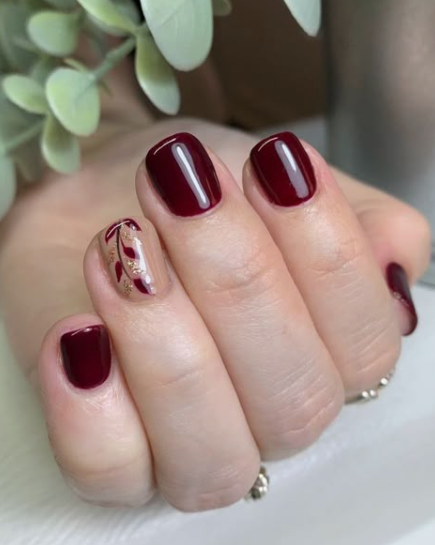 Short square nails featuring rich burgundy nail designs alongside an accent nail with a nude base, delicate burgundy leaf patterns, and gold flake details.
