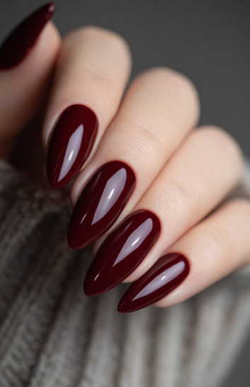 Sophisticated almond-shaped burgundy nail designs showcasing a glossy, deep dark red manicure against a knit sweater.