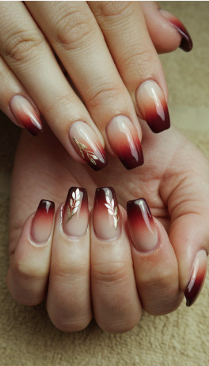 Stunning burgundy nail designs featuring a smooth dark red ombre fade into a nude base, complemented by delicate metallic gold leaf accent patterns.