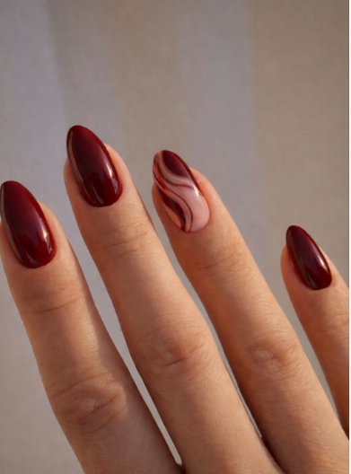 Glossy almond-shaped burgundy nail designs featuring solid deep dark red nails paired with an accent nail showing delicate abstract swirls on a nude base.