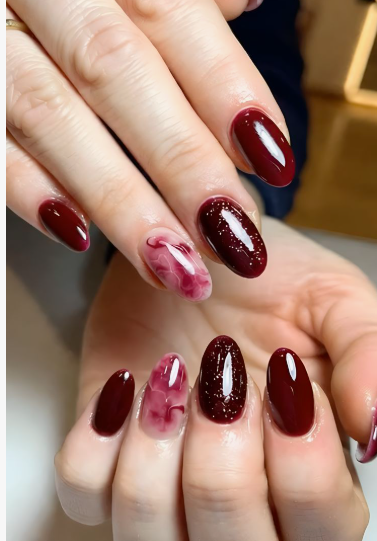 Beautiful oval-shaped burgundy nail designs featuring a mix of solid dark red polish, fine glitter accents, and a translucent marble-effect accent nail.
