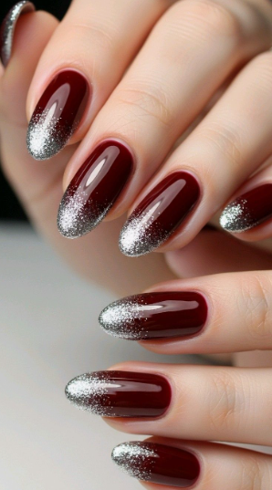 Glamorous oval-shaped burgundy nail designs featuring a glossy deep dark red base with a sparkling silver glitter ombre fade at the tips.