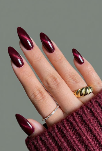 Stunning long almond-shaped burgundy nail designs featuring a mesmerizing cat-eye magnetic shimmer effect in deep maroon polish.