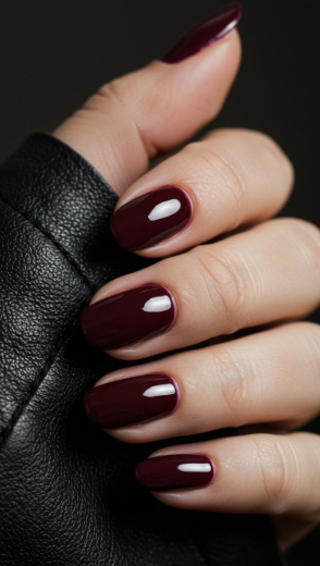 Sleek short square burgundy nail designs featuring a high-gloss, deep maroon finish next to a black leather jacket