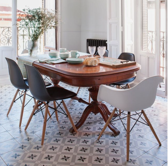 Vintage Modern Home Decor Ideas: 15 Ways to Mix Old and New "Bright dining room blending Vintage Modern Home Decor Ideas, featuring an ornate wooden extendable table, mixed modern molded chairs with wooden legs, patterned floor tiles, and tall windows."